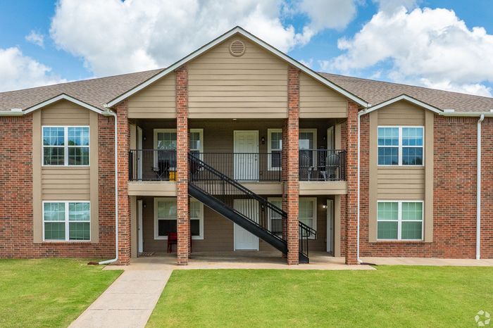 Charming brick apartment building with manicured lawn and inviting balconies under a bright blue sky.
