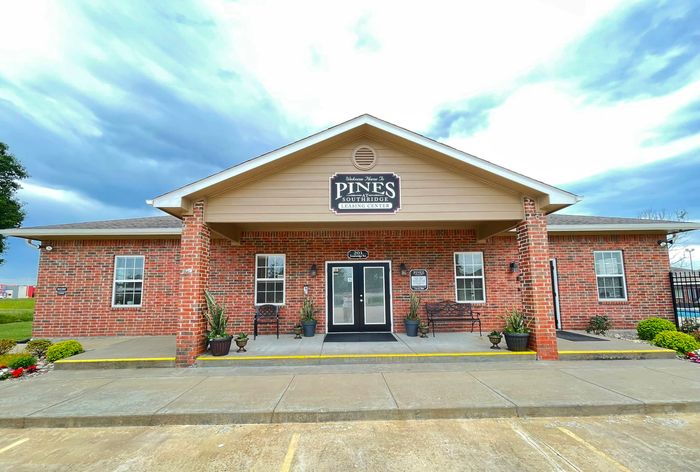 Charming leasing center with rustic red brick facade, inviting entryway, and landscaped surroundings under a vibrant blue sky at The Pines.