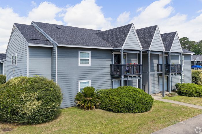 Charming gray duplex with modern architecture, featuring gabled roofs and cozy balconies, surrounded by lush greenery.