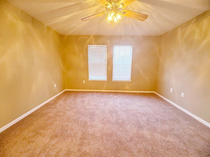 Bright and spacious room with plush carpet, elegant ceiling fan, and double windows providing natural light.