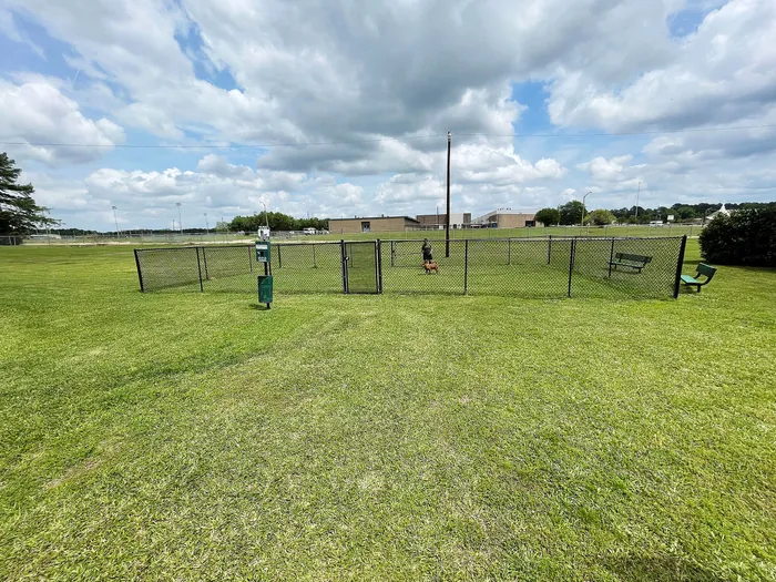 Open green space with a fenced dog park featuring benches under a picturesque sky.
