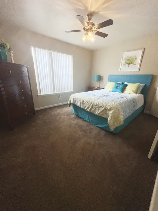 Cozy bedroom with a modern ceiling fan, featuring a plush bed with decorative pillows, soft carpeting, and a stylish dresser.