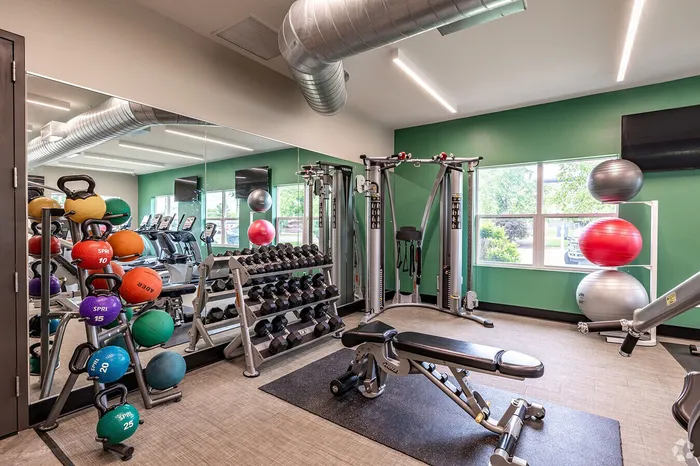 Modern gym with state-of-the-art equipment, featuring kettlebells, dumbbells, and exercise balls in a well-lit space with large windows.