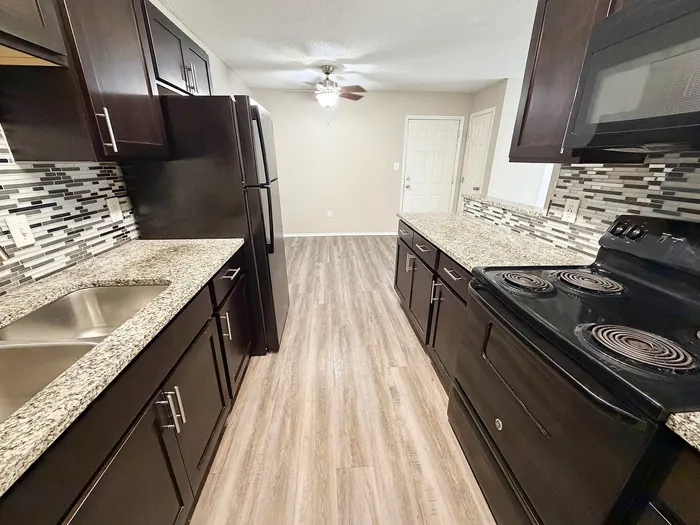 Modern kitchen with sleek dark cabinetry, granite countertops, stylish backsplash, and stainless steel sink, showcasing an elegant interior design.
