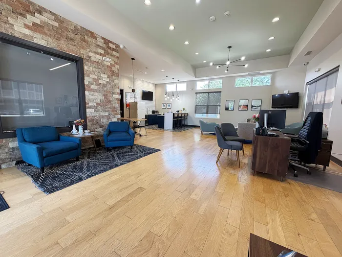 Modern and spacious apartment lounge featuring stylish blue armchairs, a chic accent wall, and a welcoming open-concept ambiance with natural light.