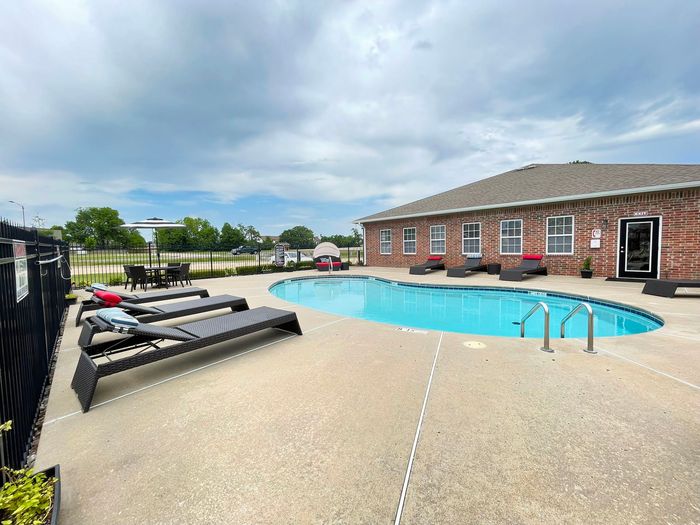 Inviting outdoor pool area with modern lounge chairs and brick clubhouse, perfect for relaxing in a serene environment.