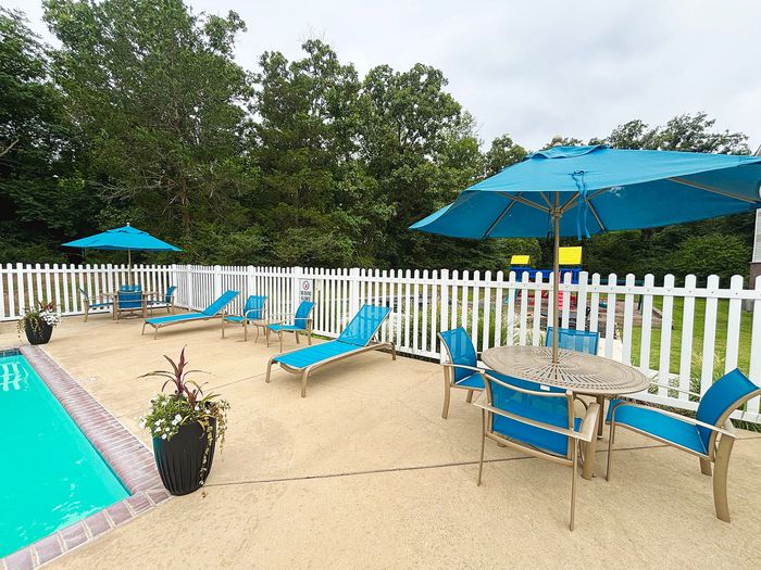 Inviting outdoor pool area with vibrant blue lounge chairs and umbrellas surrounded by lush greenery, perfect for relaxation.