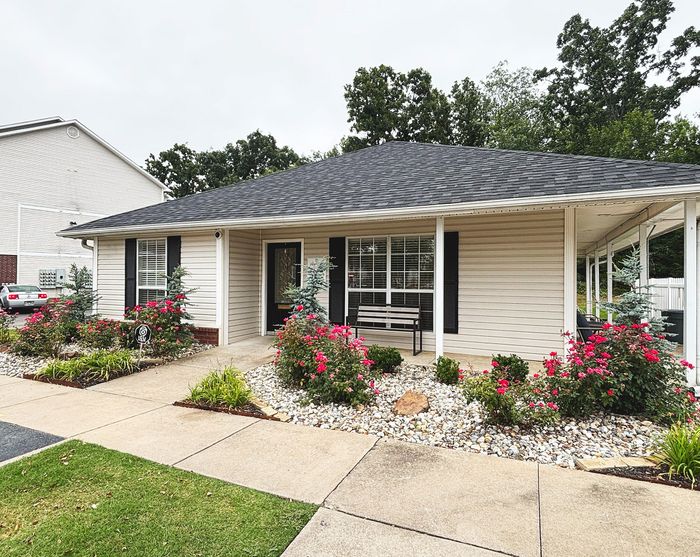 Charming single-story home with a welcoming porch, surrounded by vibrant shrubbery and rose bushes, ideal for tranquil living.