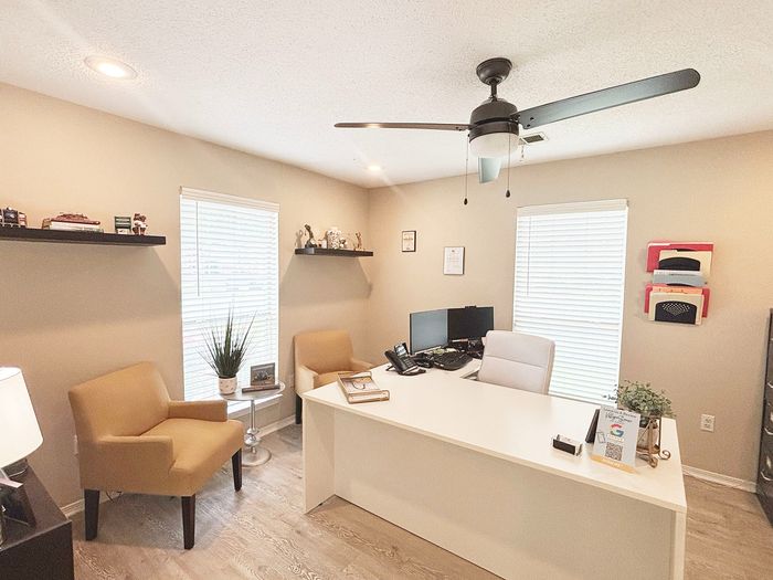 Modern home office with stylish beige chairs, a sleek white desk, vibrant decor, and ample natural light.