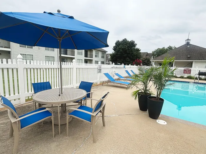 Inviting outdoor pool area with stylish lounge chairs, vibrant blue umbrella, and lush greenery, perfect for relaxation and social gatherings.