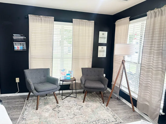 Inviting modern living space with cozy armchairs, a stylish floor lamp, and natural light streaming through large windows.