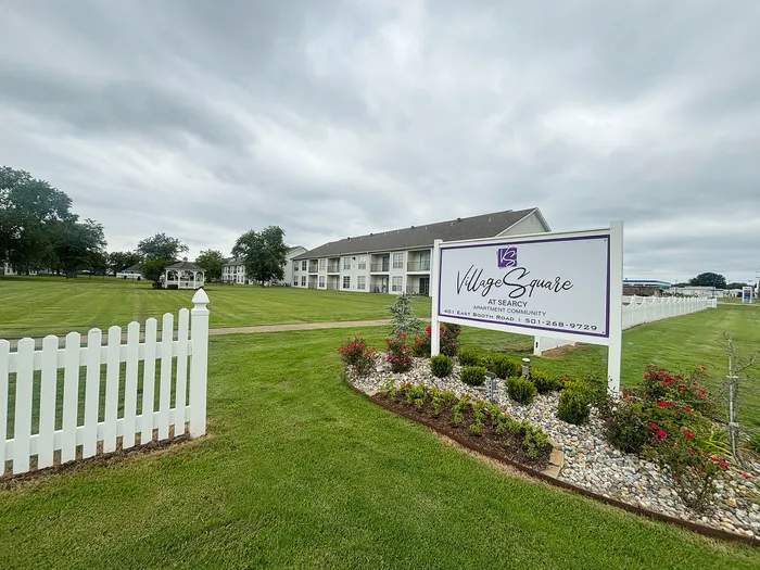 Charming apartment community in Searcy featuring manicured lawns, a white picket fence, and beautifully landscaped gardens.