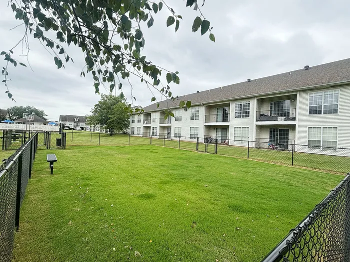 Charming apartment complex with spacious fenced yard, lush green lawn, and inviting balconies.