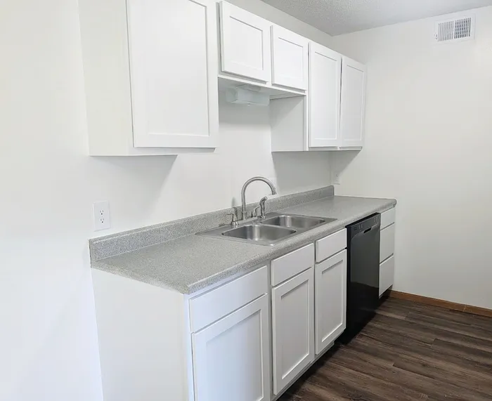 Modern kitchen with sleek white cabinets, glossy countertops, and stainless steel sink, complemented by warm wood flooring.