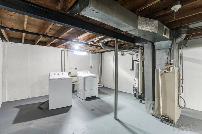 Bright, functional basement laundry room with modern washer and dryer, featuring exposed wooden beams and clean, spacious layout.