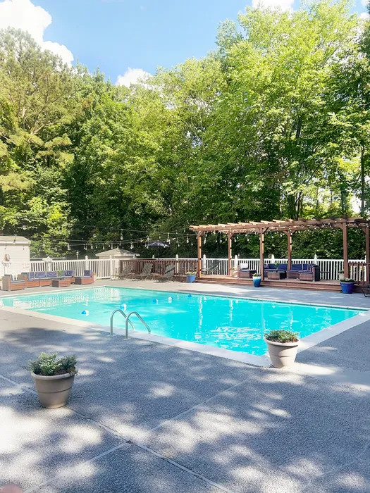 Inviting outdoor pool area surrounded by lush greenery, featuring a pergola and cozy seating under bright blue skies.