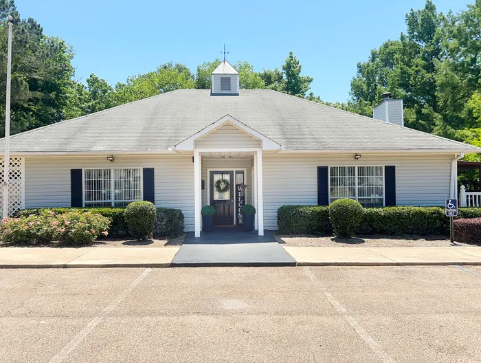 Charming single-story building with a welcoming entrance, lush landscaping, and accessible parking, ideal for community living.