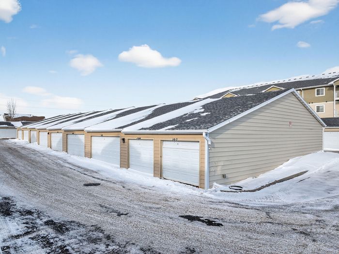 Row of modern garages with snow-covered roofs offering convenient and secure parking, set against a clear blue winter sky.