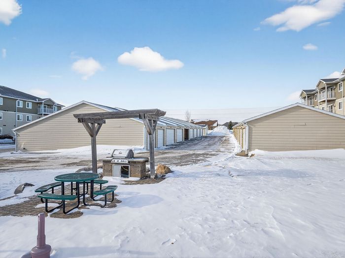 Charming winter landscape showcasing stylish garages, cozy outdoor seating, and a modern grill, perfect for enjoying the serene snowy setting.