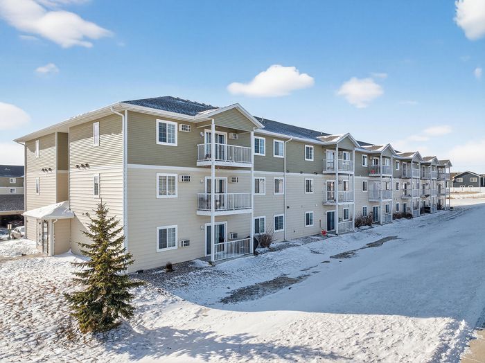 Modern multi-story apartment building with inviting balconies, set against a clear blue sky with snowy surroundings.