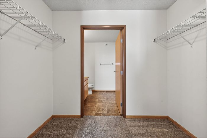 Bright walk-in closet with ample shelving, leading to a modern bathroom with elegant tiling.