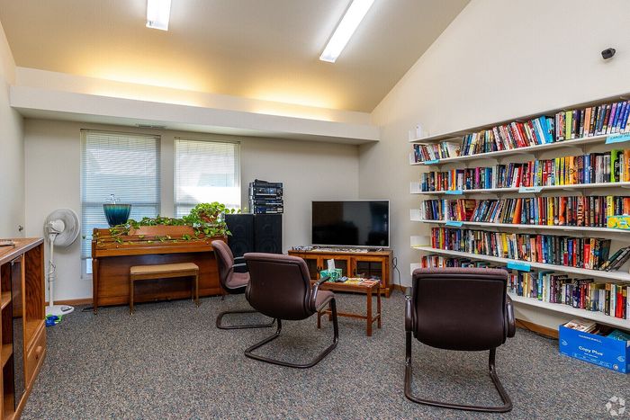 Inviting reading room with abundant natural light, complemented by a cozy seating area, a stylish piano, and an extensive bookshelf lined with colorful books.