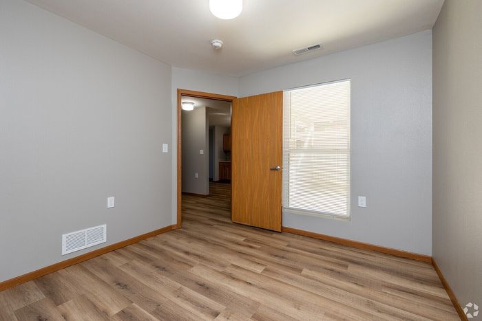 Bright and inviting room boasting elegant wood flooring, a large window for natural light, and a warm wooden door.