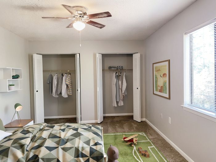 Bright bedroom featuring a cozy bed with geometric bedding, dual closets, and modern decor, ideal for comfort and style.