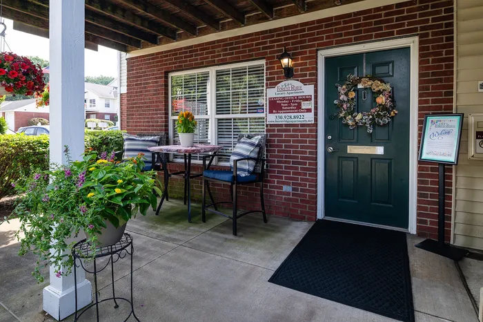 Charming apartment entrance with a cozy patio featuring vibrant plants, a stylish table setting, and a welcoming door adorned with a floral wreath.