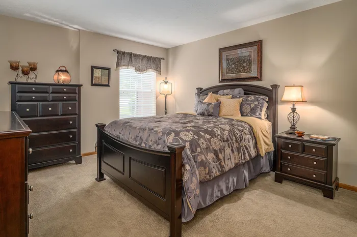 Elegant bedroom with a chic dark wood bed frame, plush floral bedding, and matching dresser and nightstand, bathed in natural light.