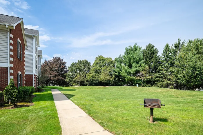 Inviting outdoor area with lush green lawn and charming red brick apartments, featuring a barbecue grill for a perfect community gathering spot.