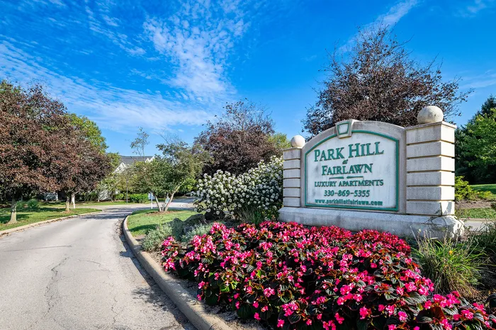 Inviting entrance to Park Hill at Fairlawn with vibrant landscaping and a clear blue sky, offering luxury apartment living.