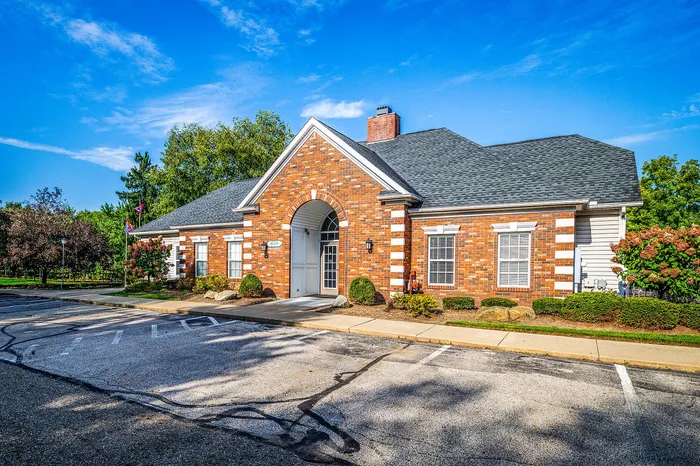 Charming brick building with a gabled roof, inviting front entry, lush landscaping, and spacious parking under a clear blue sky.