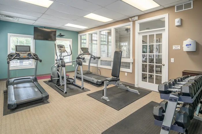 Inviting fitness center with modern treadmills, stationary bike, weight bench, and a complete set of dumbbells in a bright, airy space.