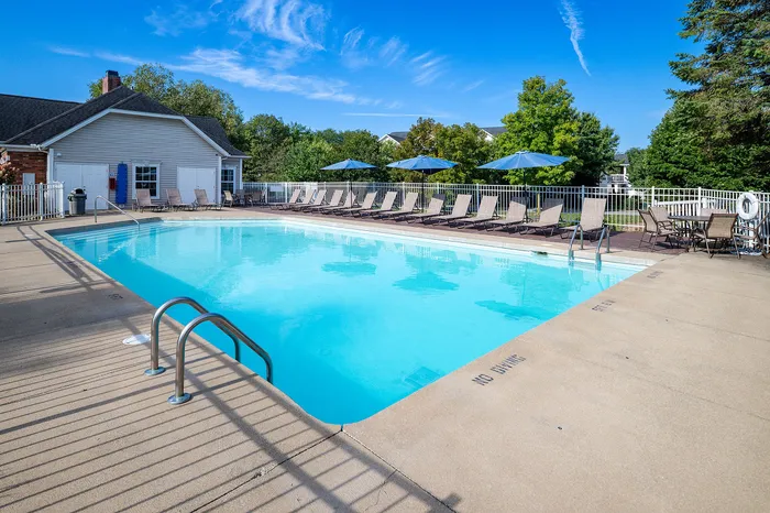 Inviting outdoor pool area with lounge chairs and umbrellas, surrounded by lush greenery and a clear blue sky.