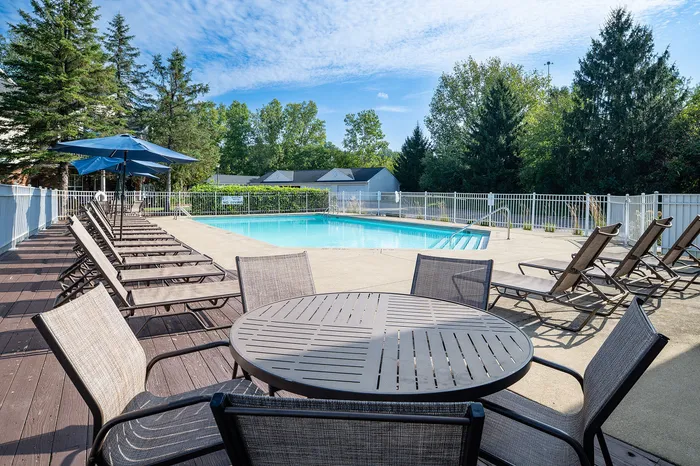 Inviting outdoor swimming pool with lounge chairs and umbrella-shaded seating, set against a backdrop of lush green trees.