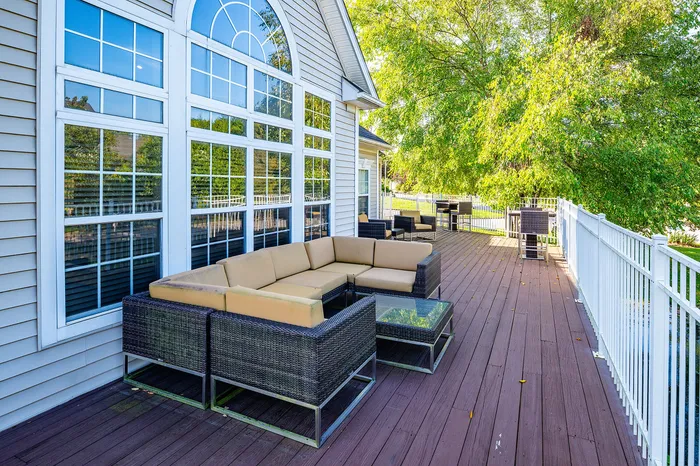 Inviting outdoor deck with plush seating, surrounded by lush greenery and elegant large windows for a serene and relaxing ambiance.
