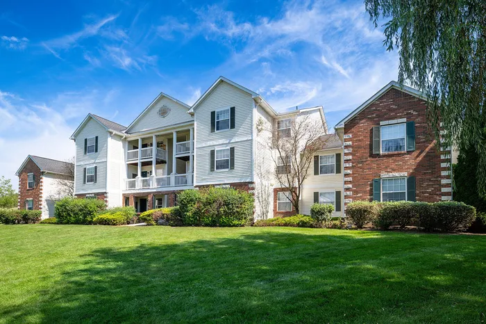 Charming apartment building surrounded by lush greenery under a vibrant blue sky, offering a serene and inviting living environment.