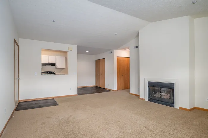 Spacious living room with cozy fireplace and open kitchen entryway, featuring warm carpet flooring and ample natural light.