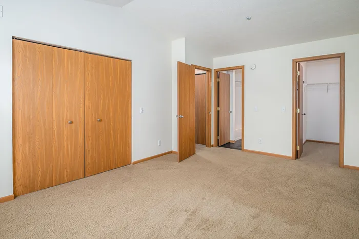 Bright room with plush carpet and warm wooden doors leading to a spacious walk-in closet, ideal for an inviting bedroom atmosphere.