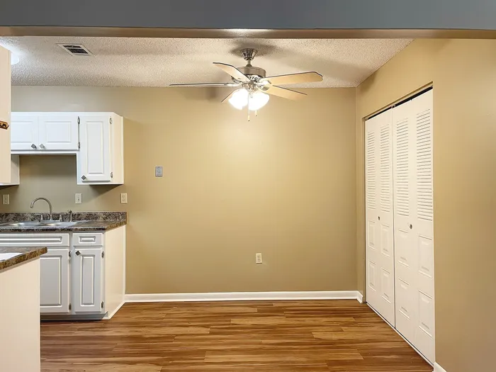 Inviting kitchen area with sleek white cabinetry, elegant wood flooring, and a ceiling fan for comfort and style.