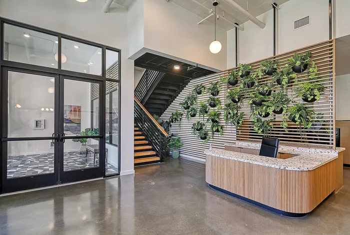 Modern lobby area with sleek design features, showcasing a green vertical plant wall, stylish seating, and an inviting staircase.