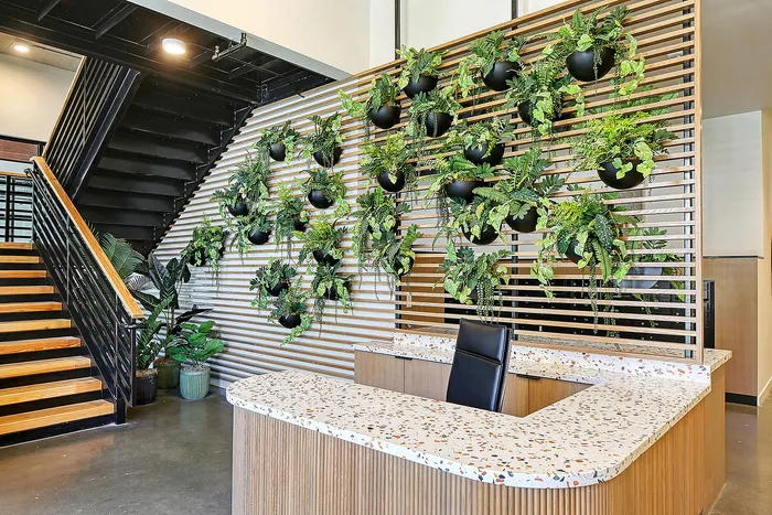 Inviting apartment lobby with a modern staircase, vibrant green wall of plants, and a sleek terrazzo reception desk.