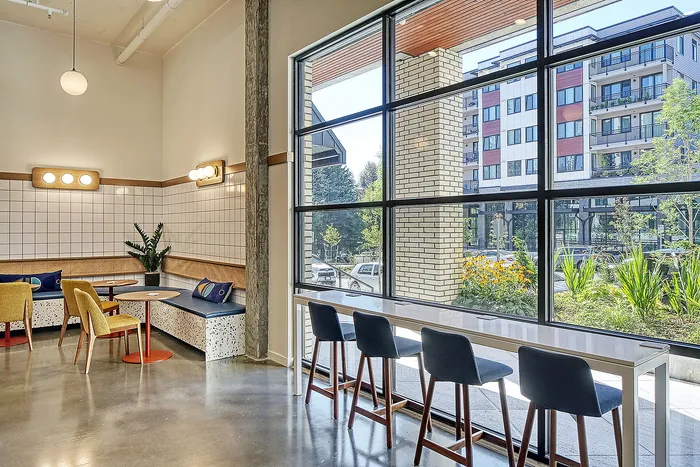 Chic urban cafe interior with stylish seating and large windows showcasing a scenic view of vibrant greenery and modern buildings.