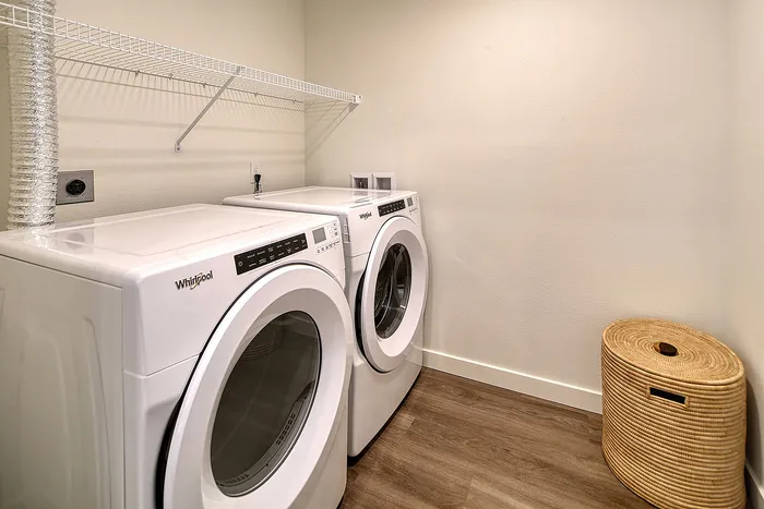Modern laundry room featuring a sleek washer and dryer with ample shelving and elegant wooden flooring.