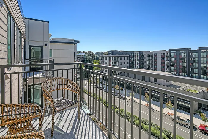 Charming apartment balcony with wicker chairs overlooking a vibrant urban landscape and modern apartment buildings.