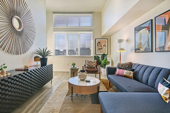 Chic modern living room with plush blue sofa, stylish decor, and large sunlit windows.