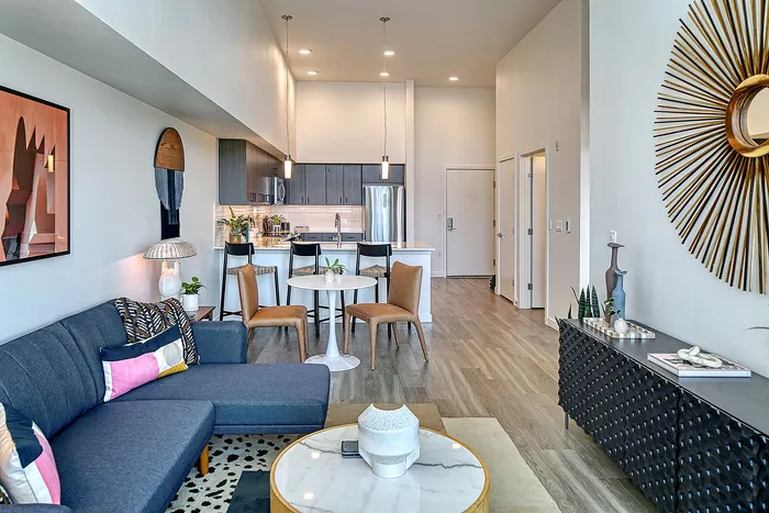 Chic open-plan living room with modern decor, sleek kitchen, and cozy dining area, featuring stylish furniture and warm lighting.