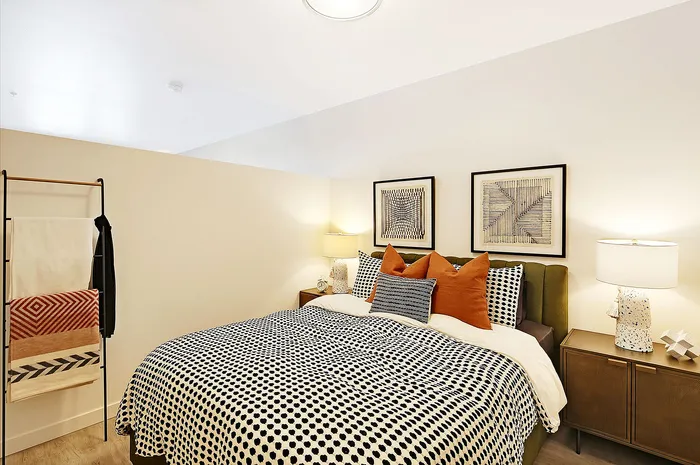 Elegant bedroom with stylish decor, featuring a cozy bed with patterned upholstery, warm lighting, and modern artwork, creating a serene and inviting atmosphere.