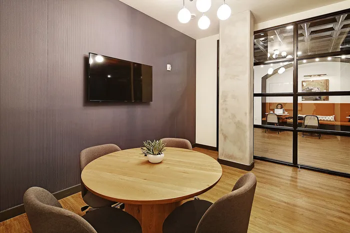 Modern meeting room with a sleek wooden table, comfortable chairs, wall-mounted TV, and a stylish glass partition.